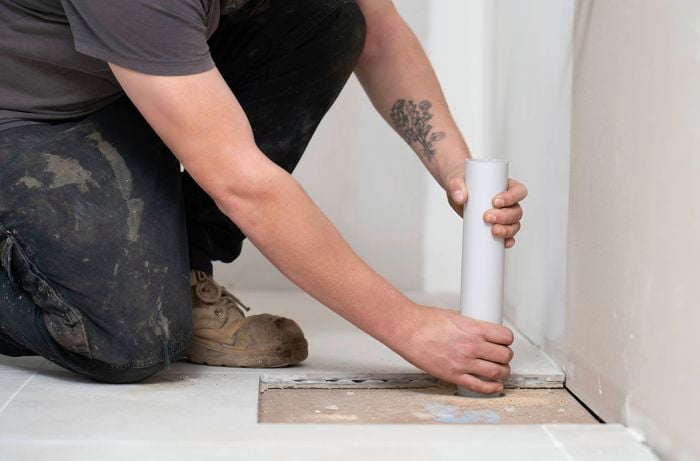 A tradesperson wearing work boots and dark pants is installing a vertical white pipe for services like plumbing and electrical.