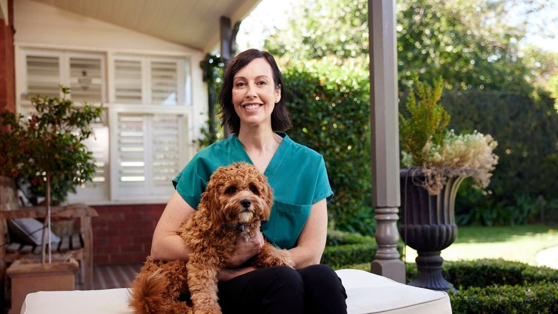 Handler and puppy sitting on a cushion in an outdoor area.
