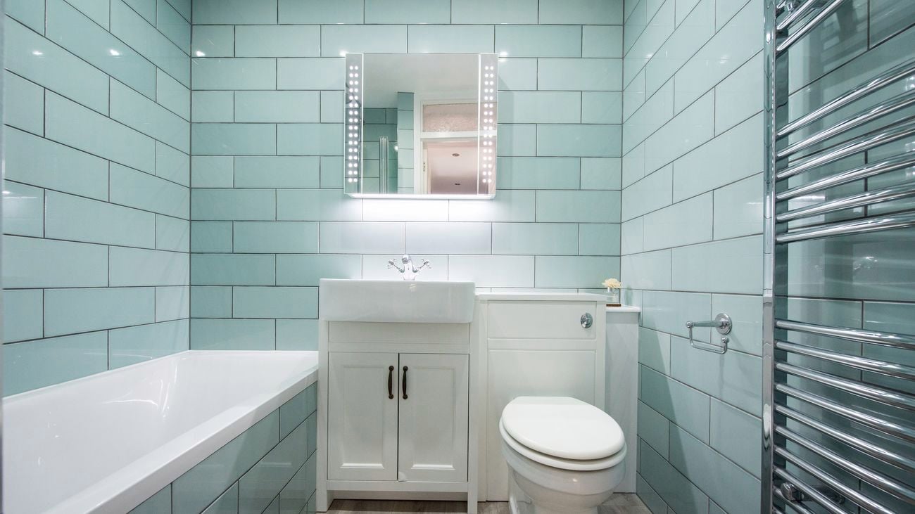 A general interior view of a small bathroom with green rectangular wall tiles.
