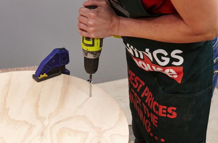 A person inserting a screw through a round table top into a table leg