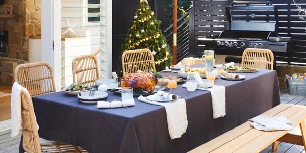 Christmas themed outdoor dining table with a Christmas tree and barbecue in background