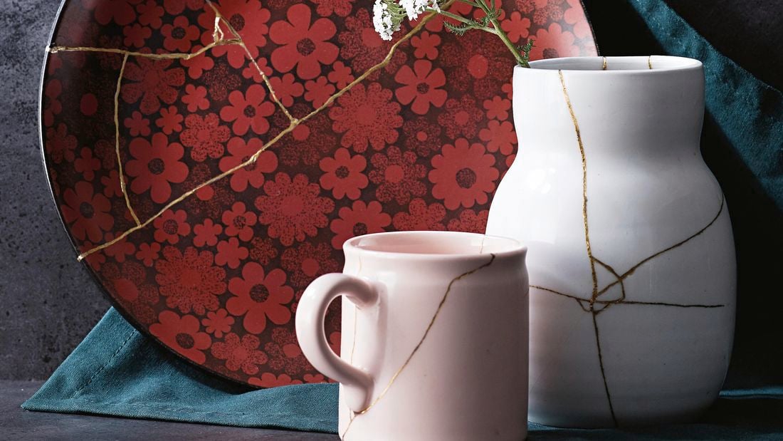 A cup, vase, and flower-patterned plate repaired with kintsugi techniques, each with a vein of gold running through