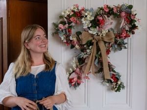 Lady standing next to finished Christmas flower bow wreath.