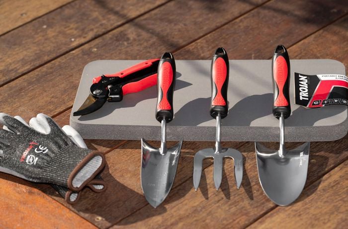  A set of gardening tools and gloves is laid out on a wooden deck, helping you choose the right gear to make potting quicker and easier.  