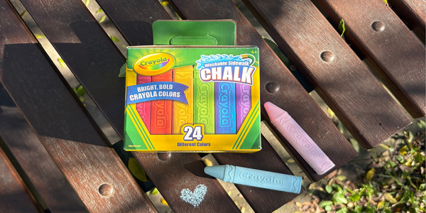 Box of Crayola washable sidewalk chalk with pastel chalk sticks displayed on a wooden outdoor table.