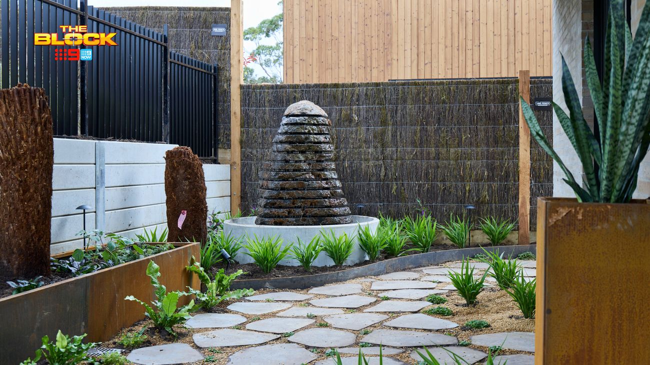Landscaped courtyard featuring a tiered stone water feature, stepping stone pathway, raised garden beds and lush greenery.
