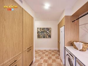 Laundry from The Block with timber cabinetry, tiled floor, washer and dryer, bench space, and wall art.