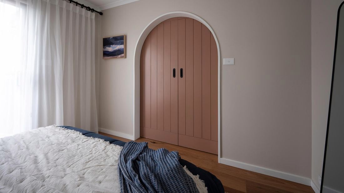 Arch frame with a clay coloured barn door in a bedroom.