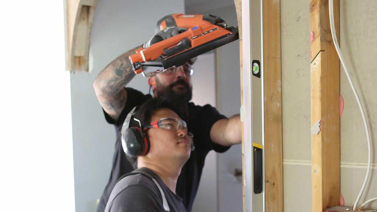 A close up image of two male carpenters, one holding a Paslode nail framer and the other in PPE holding a spirit level in place