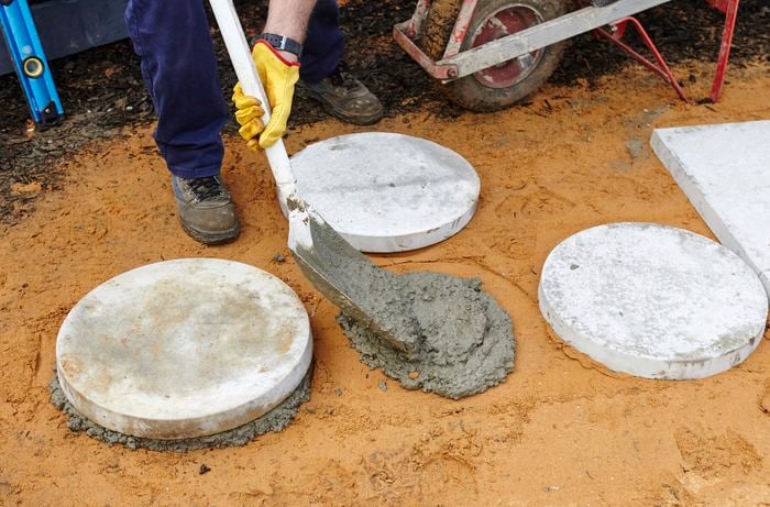 Person shovelling concrete onto a sand base between two pavers