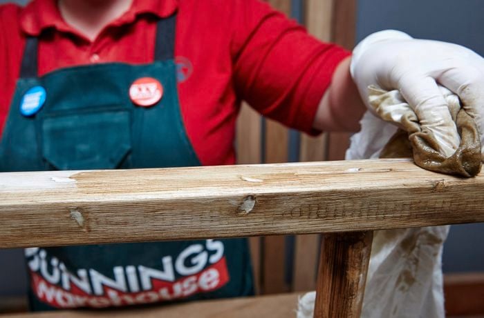 Person wiping DIY timber vintage ladder with rag and varnish.