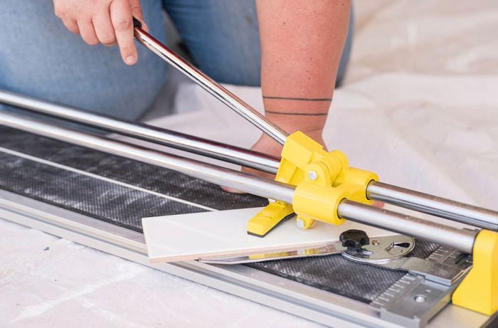 A person is using a manual tile cutter to make clean, precise cuts.