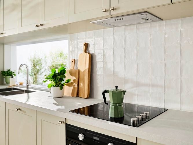 Modern beige kitchen with a benchtop, white splashback, stovetop, a plant and chopping boards on the benchtop.