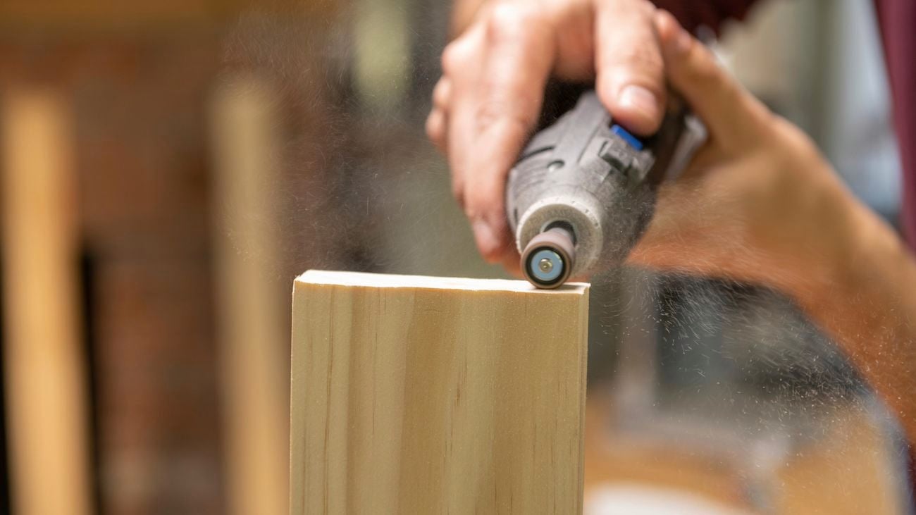 Person using the Dremel 710 160-piece multipurpose mega accessory kit to sand the edge of a plank of wood