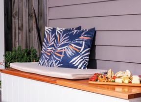 A decorated outdoor storage bench with two cushions and a fruit plater.