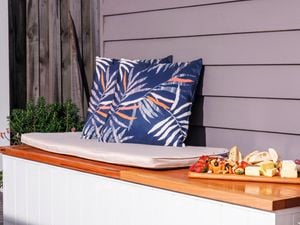 A decorated outdoor storage bench with two cushions and a fruit plater.