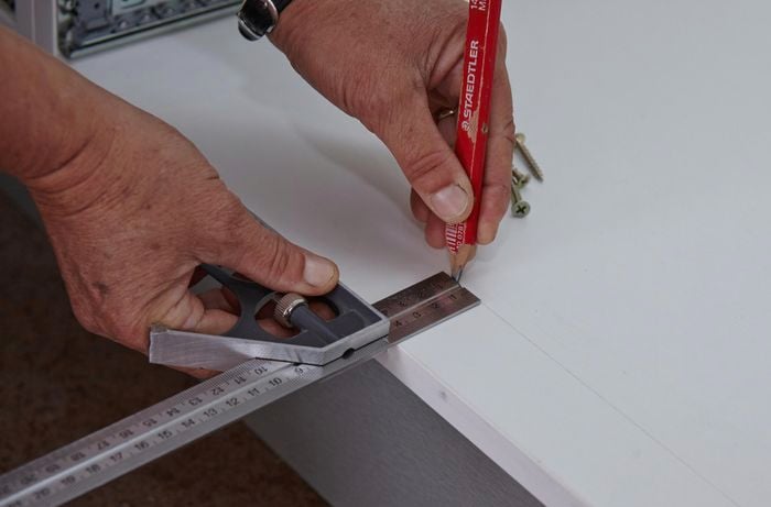 A person marking a measurement on the bottom panel of a cabinet