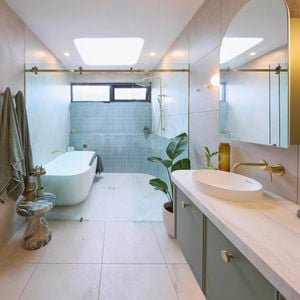 Green, gold and white coloured bathroom with a timber fluted profile vanity and marble benchtop and bath