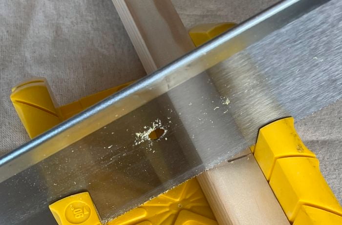 A person uses a mitre box to cut a piece of pine.