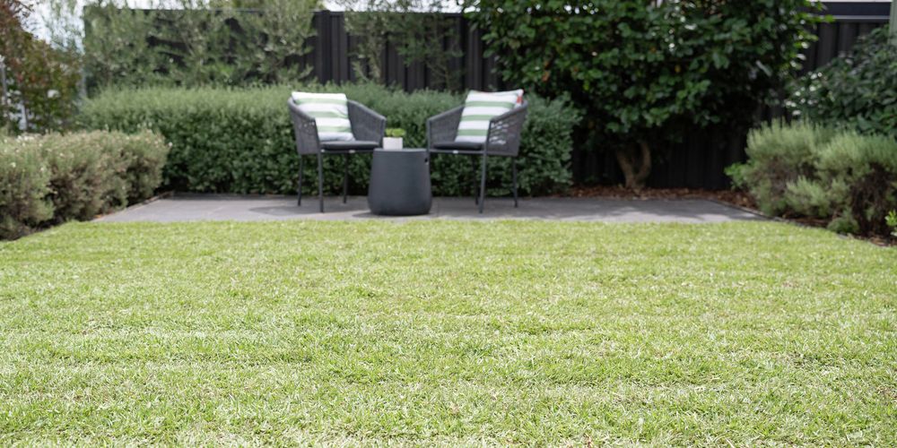 The image shows a freshly laid turf, with outdoor furniture set up on a paved area in the background.