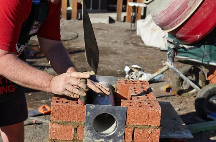 A newspaper tube being added to a brick letterbox in between an opening left in bricks
