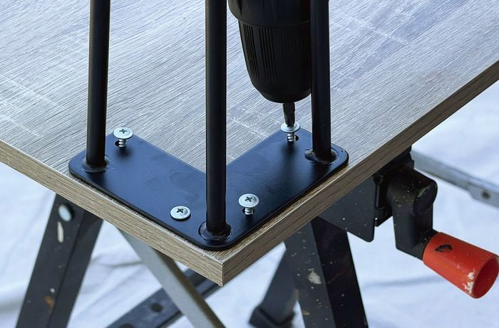  A close up image of a drill head drilling screws into a bracket of a piece of square timber.