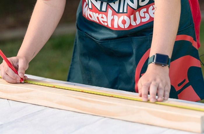 Bunnnings team member measuring a piece of timber with a measuring tape and pencil