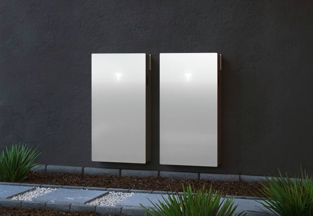 Modern house with Tesla car parked in the driveway and a tesla powerwall on the side of the house