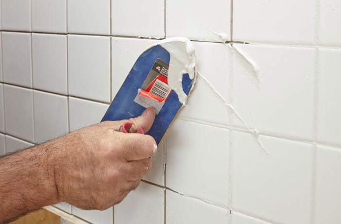 Person using scraper to apply grout to freshly tiled wall.