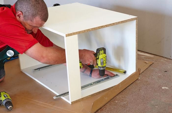 A Bunnings team member securing a basket rail to the bottom of a cabinet