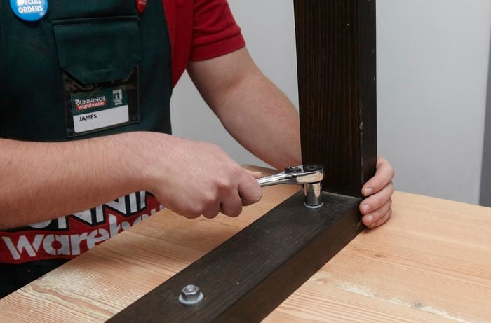 Legs being secured to the base of a wooden dining table with nuts and bolts and a ratchet