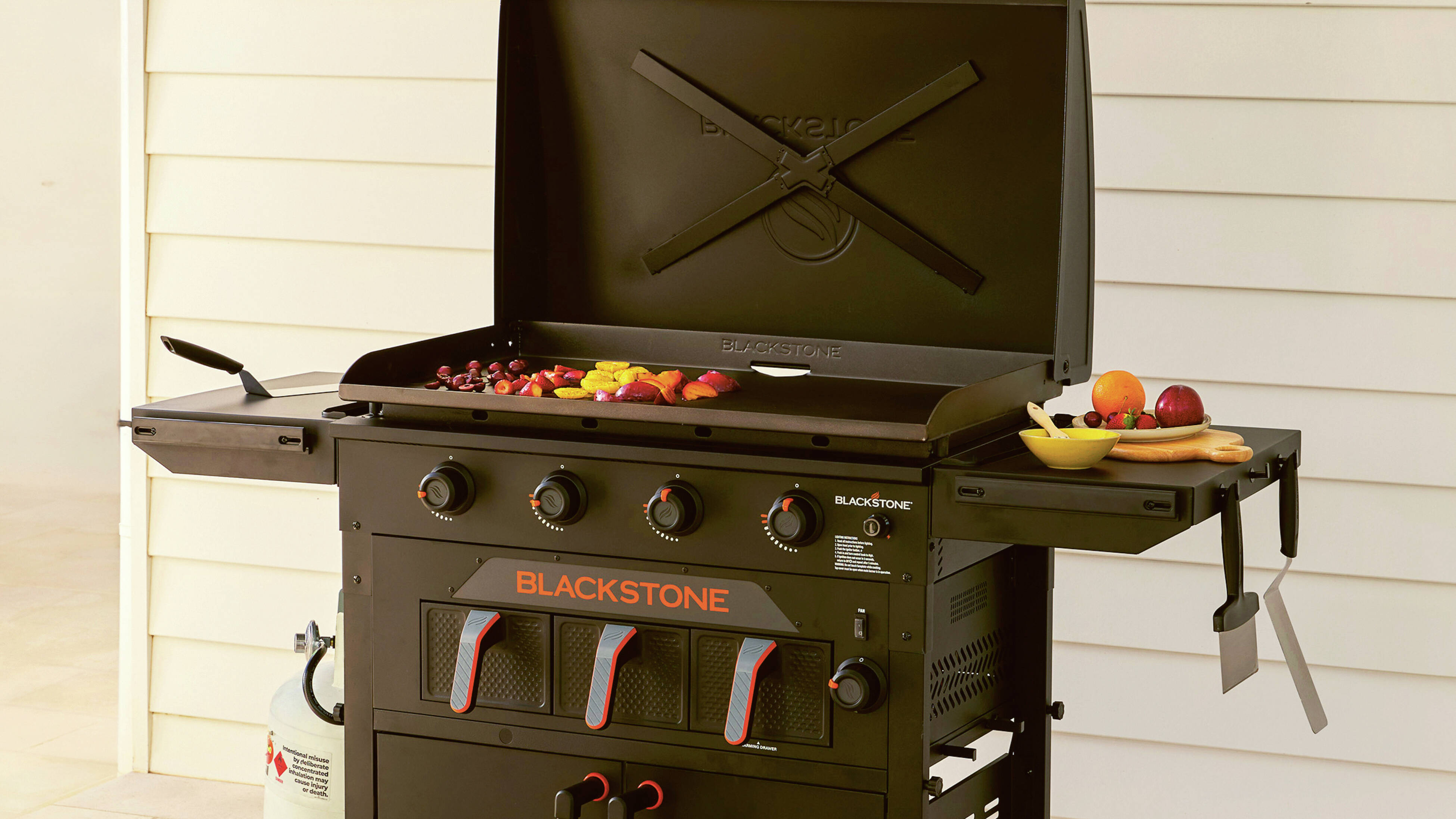 Black griddle barbecue with vegetables cooking and fruit on a side shelf