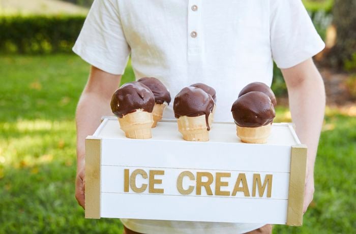 Child holding a painted wooden crate tray labelled ‘ice cream’ with chocolate-dipped ice creams on display.