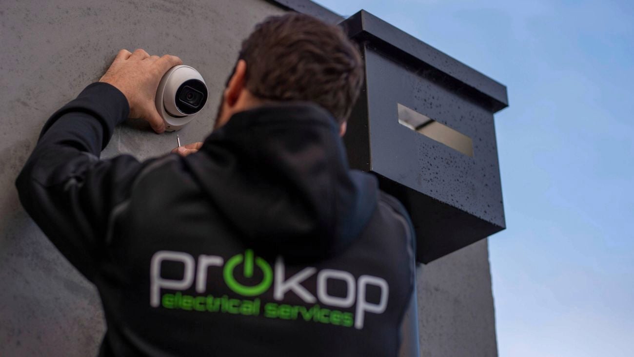 An image of a home security camera being installed by a tradesman wearing a ProKop hoodie on a ladder