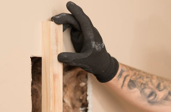 A gloved hand is measuring the length of the timber batten around the hole.