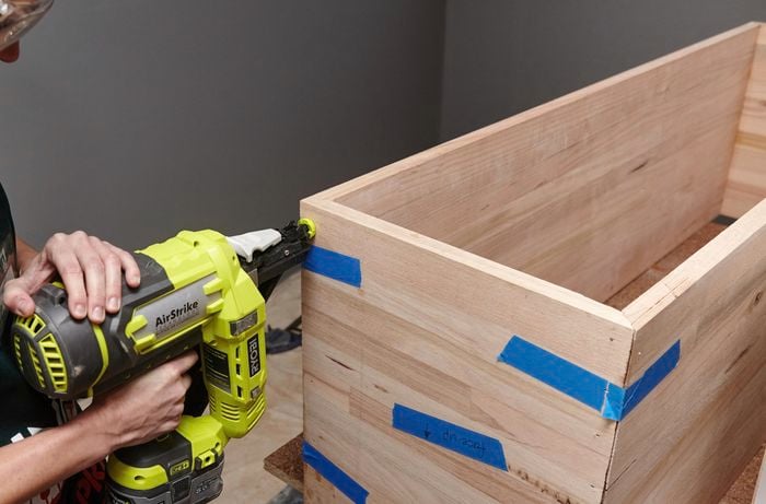 A person attaching an end piece to a timber box using a nail gun