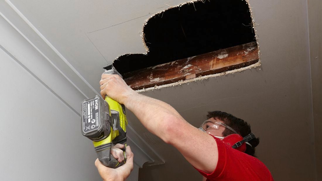 Person cutting hole in roof using jigsaw.