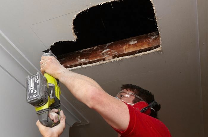 Person cutting hole in roof using jigsaw.