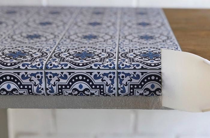 Person smoothing patterned adhesive using a plastic scraper 