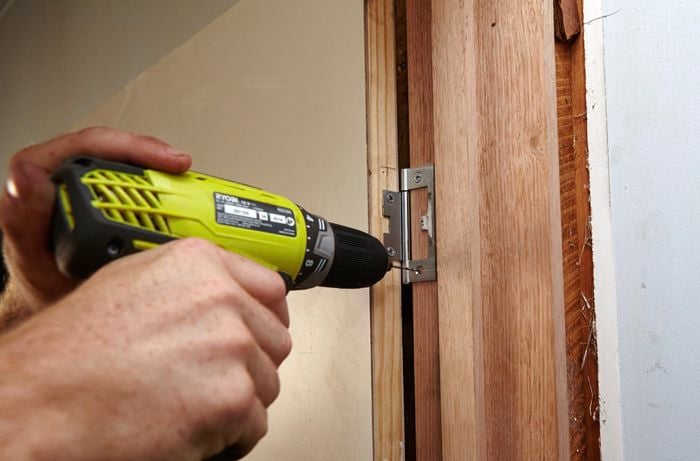 A door hinge being screwed into a doorframe using a power drill
