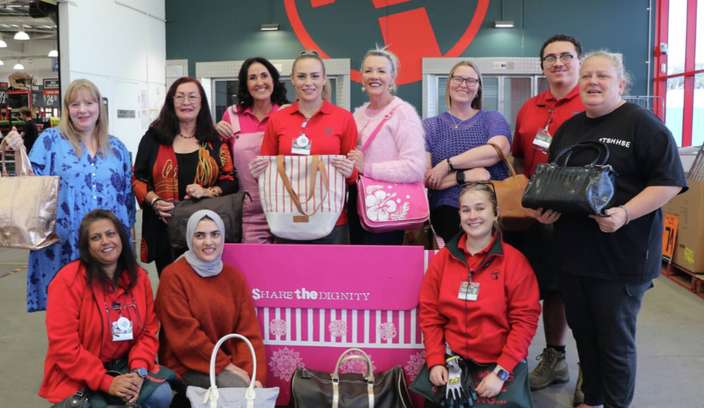 Group of Bunnings team members and volunteers holding handbags and donations in support of the Share the Dignity charity initiative.