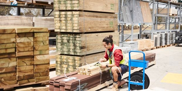 A team member securing lengths of timber to a pallet with plastic ties, in a Bunnings timber yard