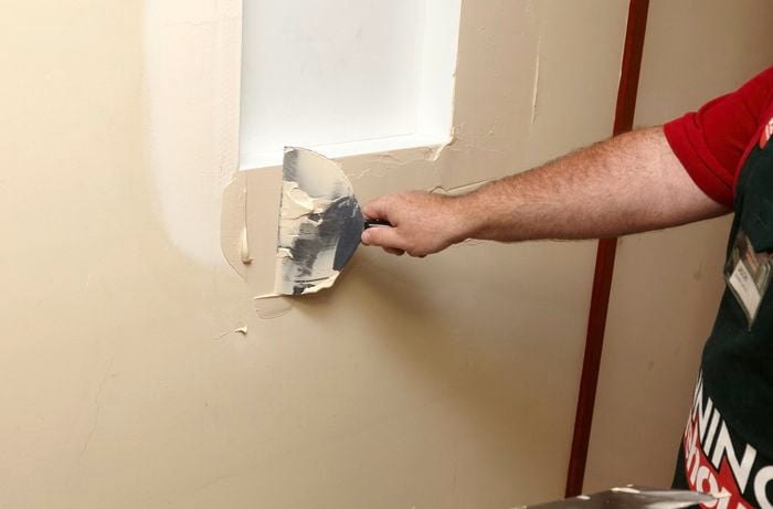 A person using a 200mm trowel to apply joint compound around a wall niche