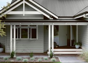 Grey house with white trim and dark corrugated iron roof, front porch with wooden deck, and garden.