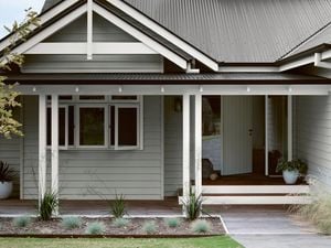 Grey house with white trim and dark corrugated iron roof, front porch with wooden deck, and garden.