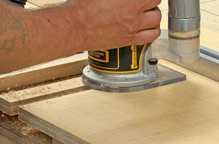 A hand operating a router to cut grooves into a piece of plywood.