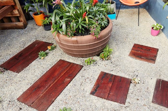 An outdoor area with timber pavers laid into white gravel amid potted plants