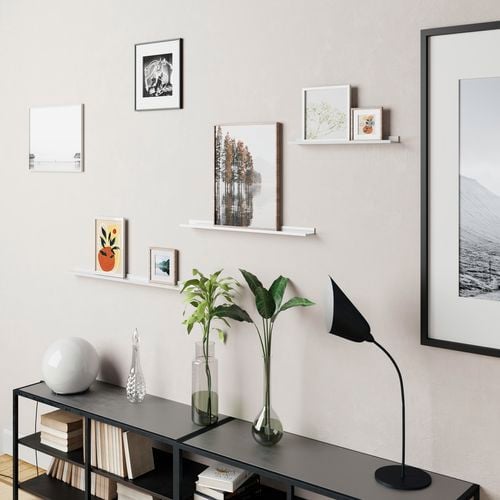 Shelving strips with prints on the wall and various vases on a floor book shelf.
