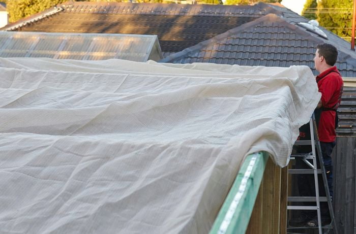 A shade cloth being stretched out over a wooden frame by a Bunnings team member on a ladder
