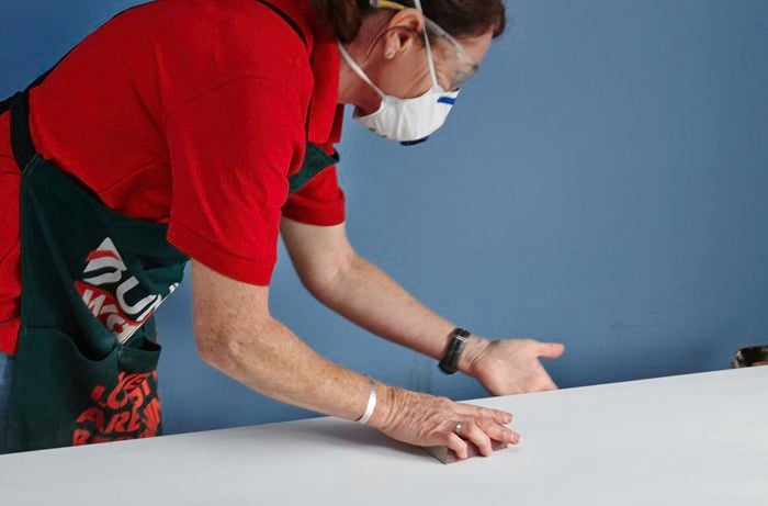 Person wearing a mask sanding a door that is lying horizontal on supports